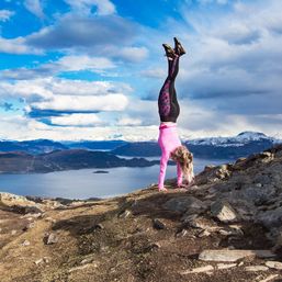 Jente i treningsklær står på hender på fjelltopp
